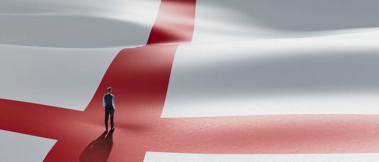 A small figure of a man stands with his back to the camera in the centre of a giant Cross of St George - the England football team's flag. The figure is dressed in Gareth Southgate's signature waistcoat, shirt sleeves and suit trousers.