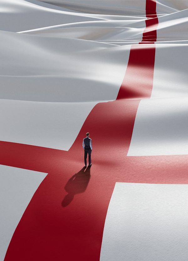 A small figure of a man stands with his back to the camera in the centre of a giant Cross of St George - the England football team's flag. The figure is dressed in Gareth Southgate's signature waistcoat, shirt sleeves and suit trousers.