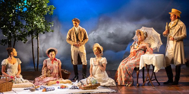 A group of men and women in Regency dress are having a picnic, with a tablecloth, baskets and food spread out. Three women are sitting on the ground, with another reclining on a chair and carrying a sunshade, next to a small table. Two men stand behind and to the side of them, carrying glasses and a wine bottle. Two trees on the left are illuminated by sunshine and the backdrop is of a blue skies with looming grey clouds