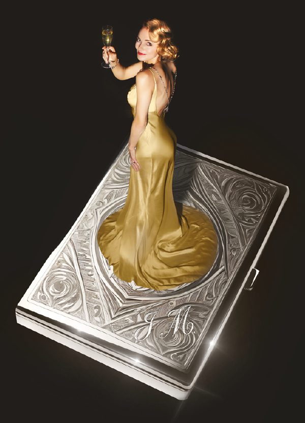 A giant, decorative, silver cigarette case floats against a black background. A young woman stands on top wearing a glamorous golden silk gown, holding a glass of champagne and looking to the camera with a smile. Her golden hair is curled and she wears red lipstick.