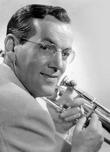 A black-and-white photograph of a man with a vintage comb over holding a trumpet, looking back over one shoulder and smiling warmly.