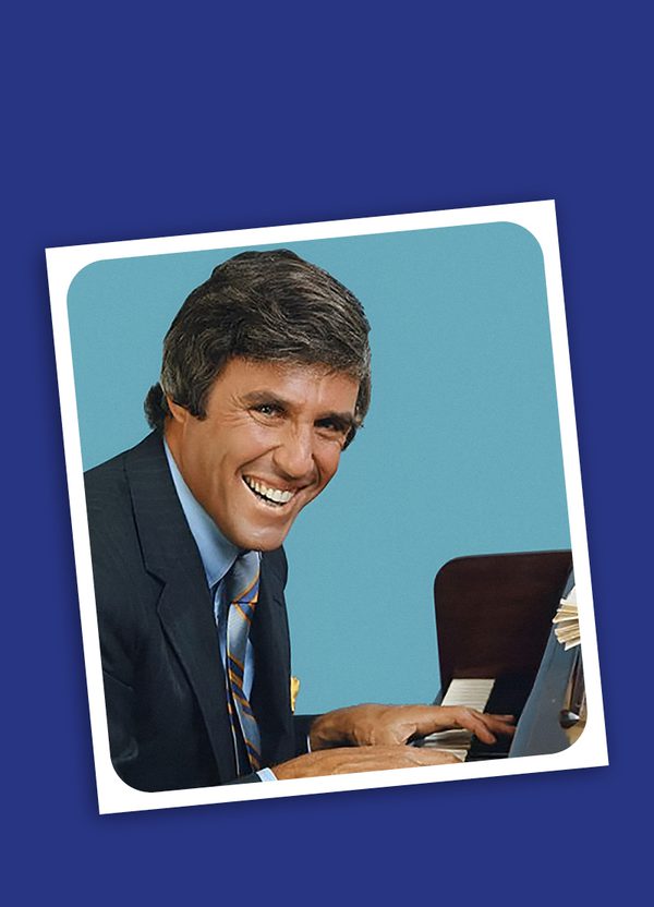 A dark blue background with a tilted photo in the middle. In the photo, is a man in a suit sat at a piano. He is looking at the camera and smiling widely. Behind him is a light blue background with rounded corners and has a white border.