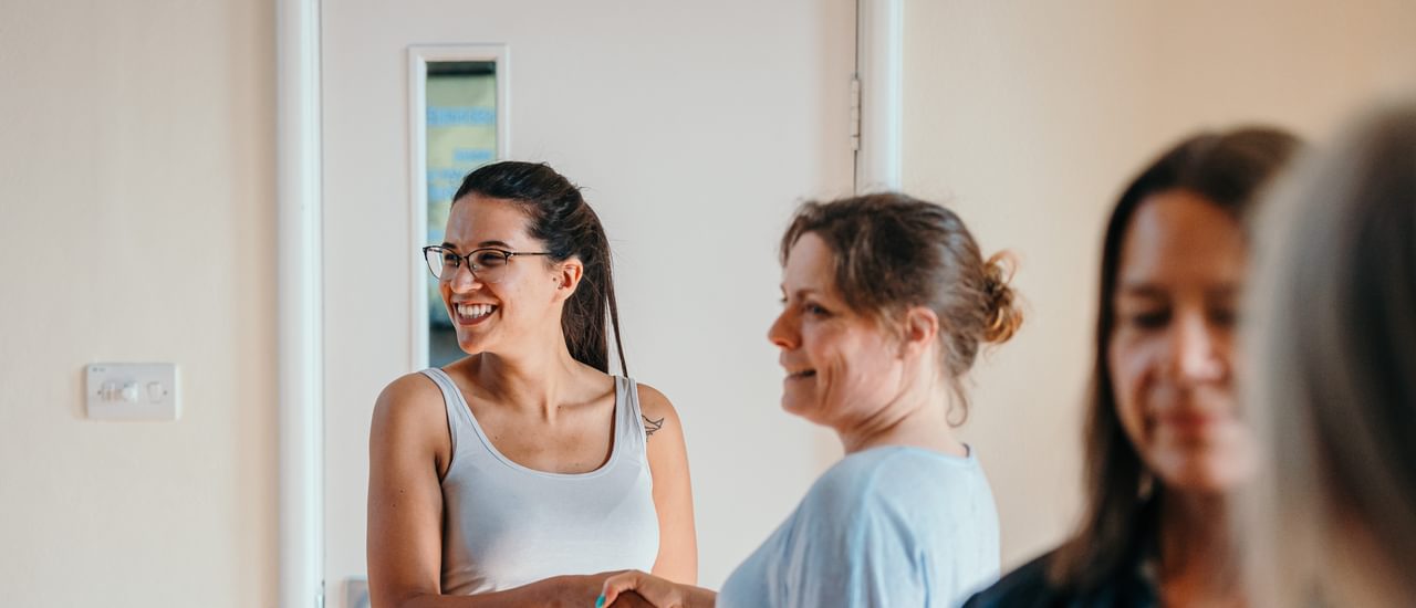 A group of people in a rehearsal space, shaking hands and smiling.