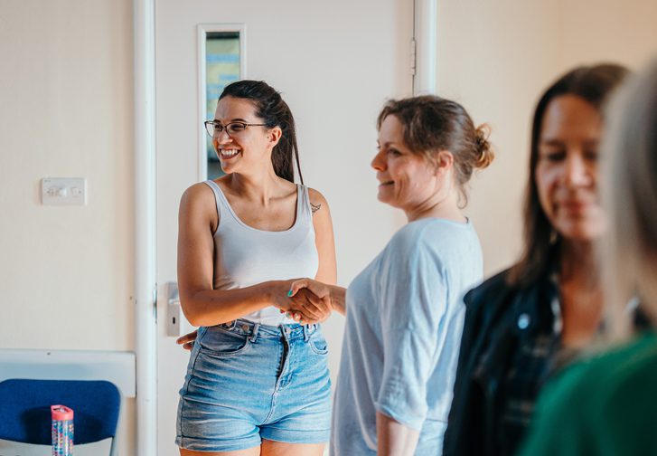 A group of people in a rehearsal space, shaking hands and smiling.