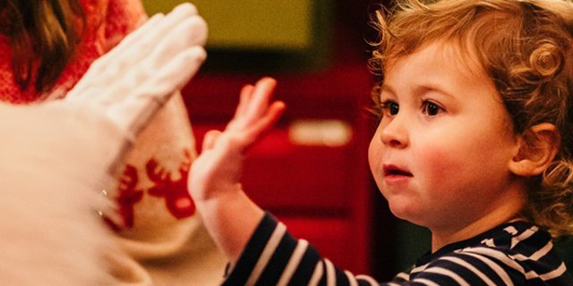 A small child 'high-fives' Santa in a sparkly grotto.
