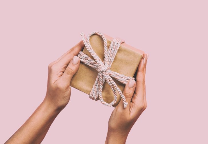 Two hands holding a brown paper package, tied up with string on a pastel pink background